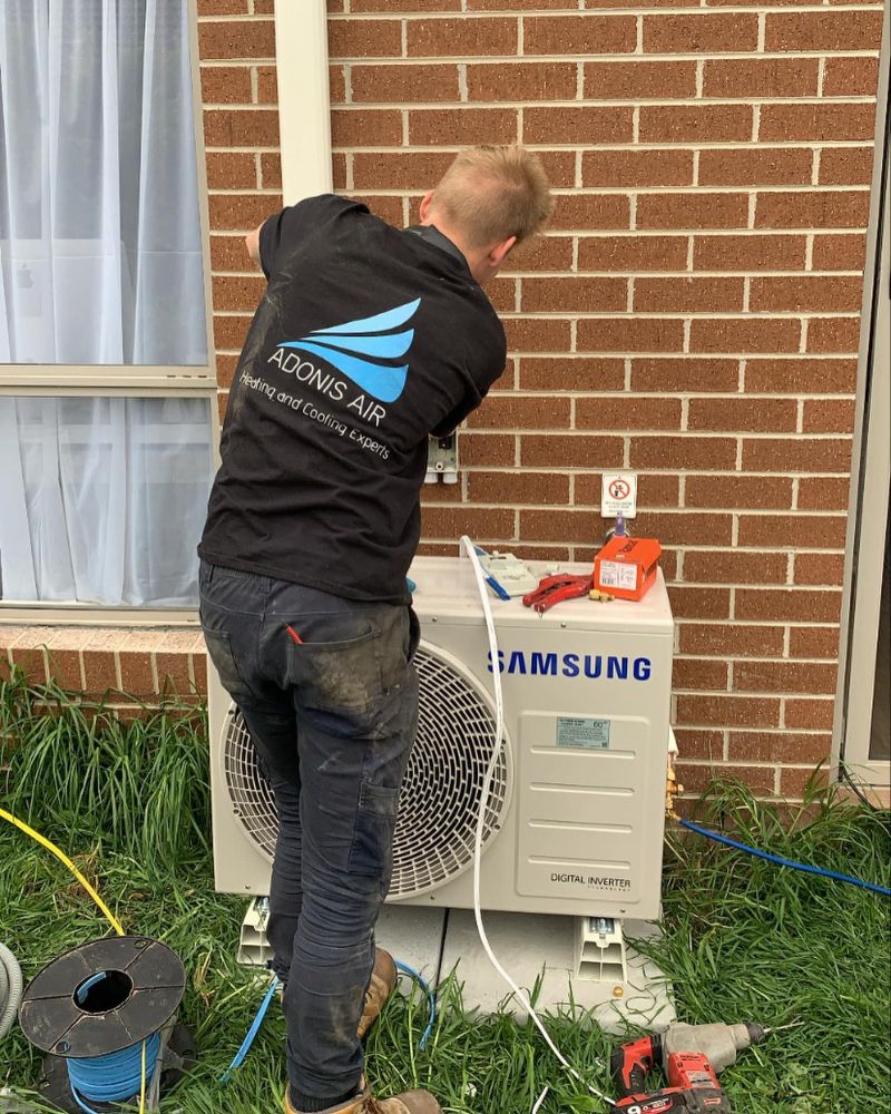 Technician working on a Samsung outdoor air conditioner beside a brick wall