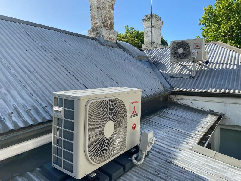 Two outdoor air conditioning units on a corrugated iron roof beside old chimneys