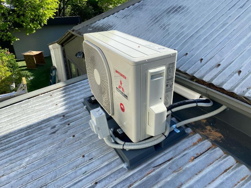 Outdoor air conditioning unit on a raised stand on a corrugated iron roof