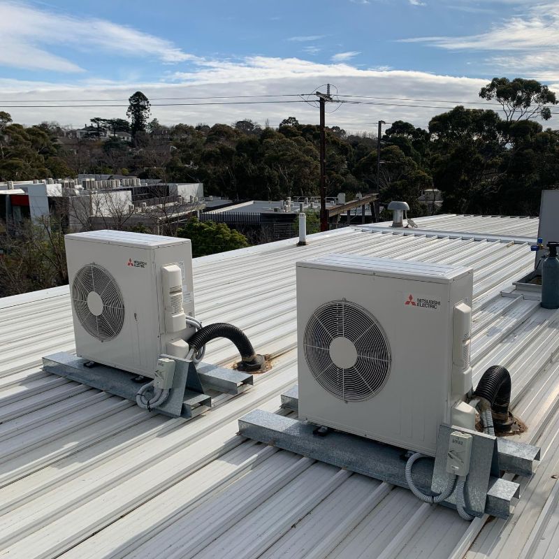 Two outdoor air conditioning units on steel frames on a metal roof