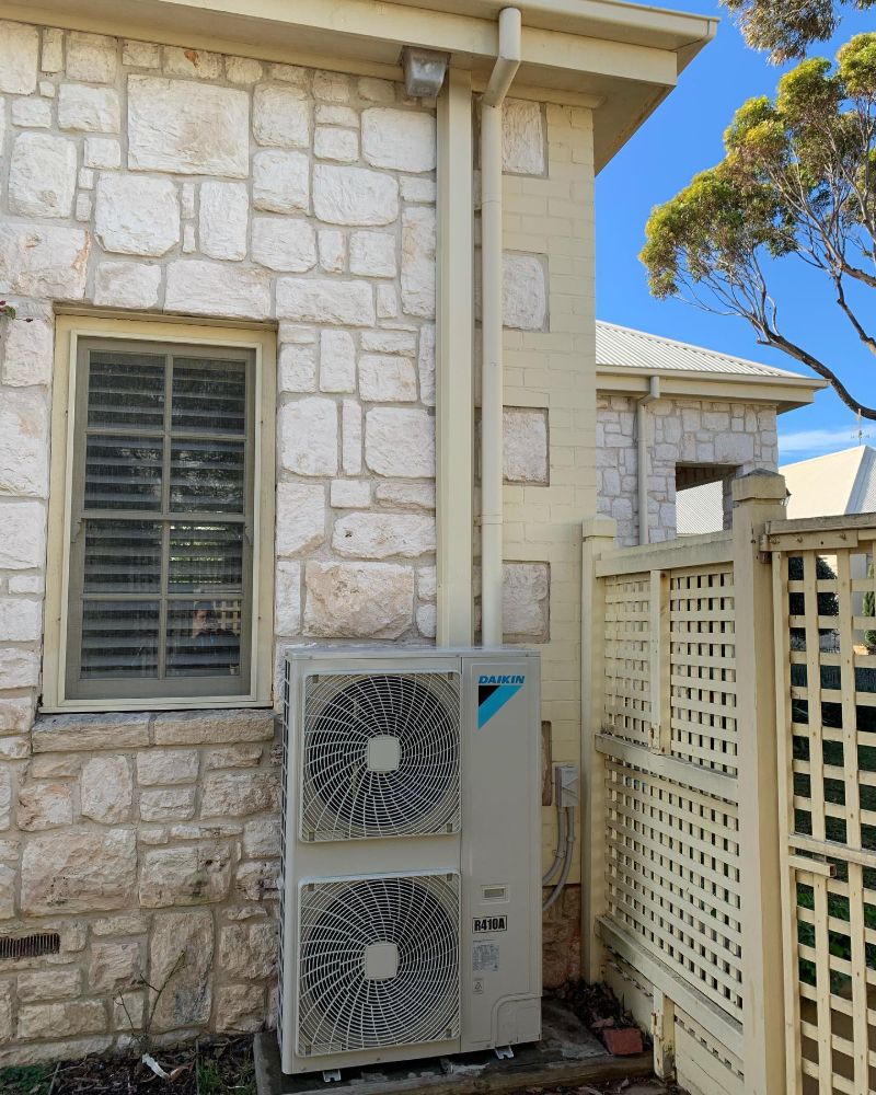 Large outdoor air conditioning unit beside a sandstone house and timber lattice