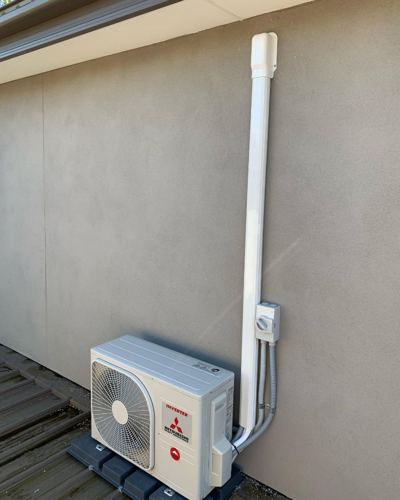 Outdoor air conditioning unit on a timber deck beside a rendered wall