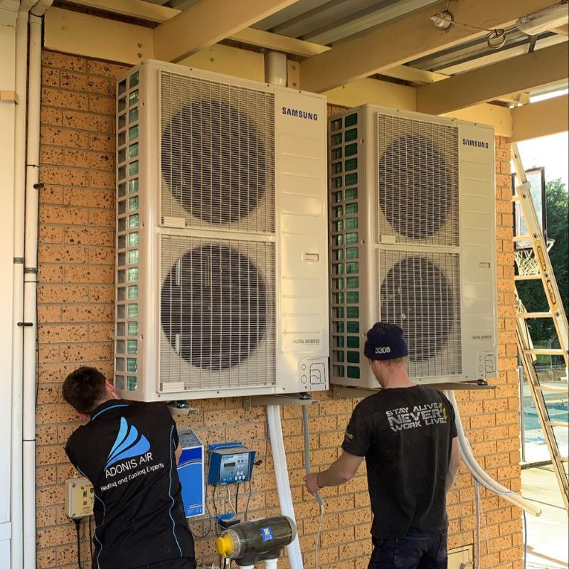 Two technicians working on large Samsung outdoor units under a pergola
