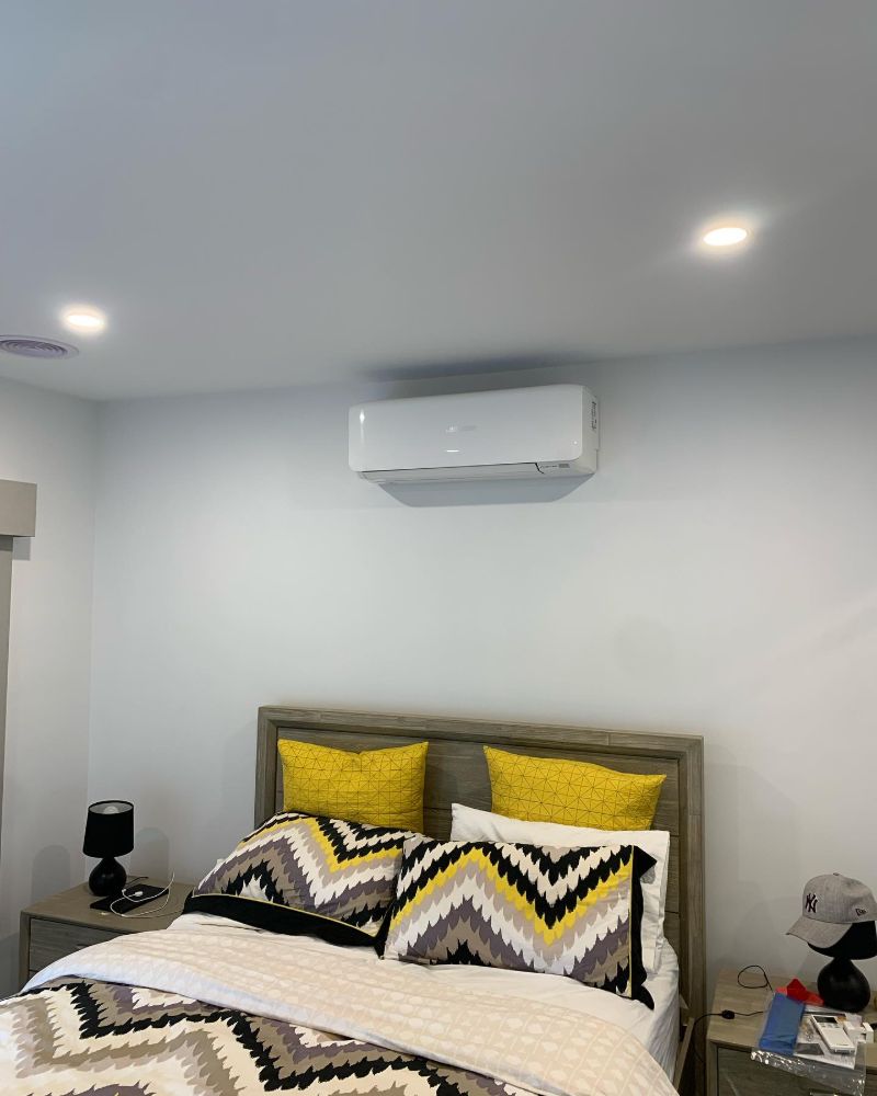 Split system air conditioner on a bedroom wall above the bed