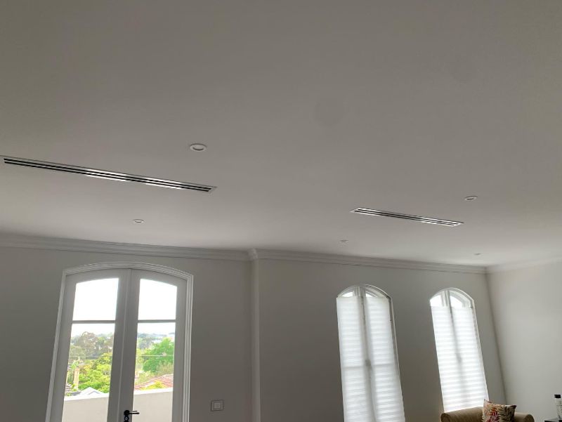 Two ducted slot vents in the ceiling of a room with arched windows
