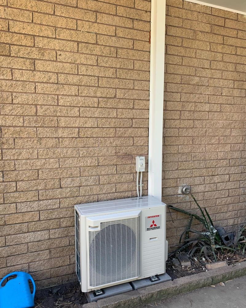 Outdoor air conditioning unit on a slab beside a cream brick wall