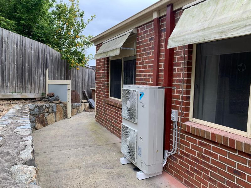 Large two-fan outdoor unit along the side path of a red brick house