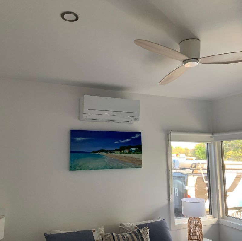 Split system air conditioner on a living room wall beside a ceiling fan