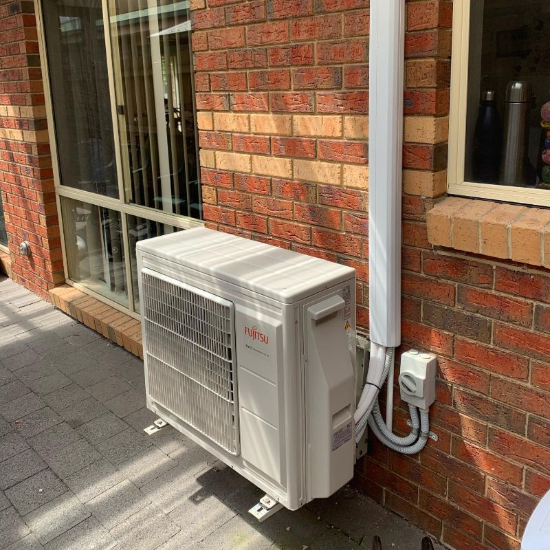 Fujitsu outdoor unit on paving beside a brick wall