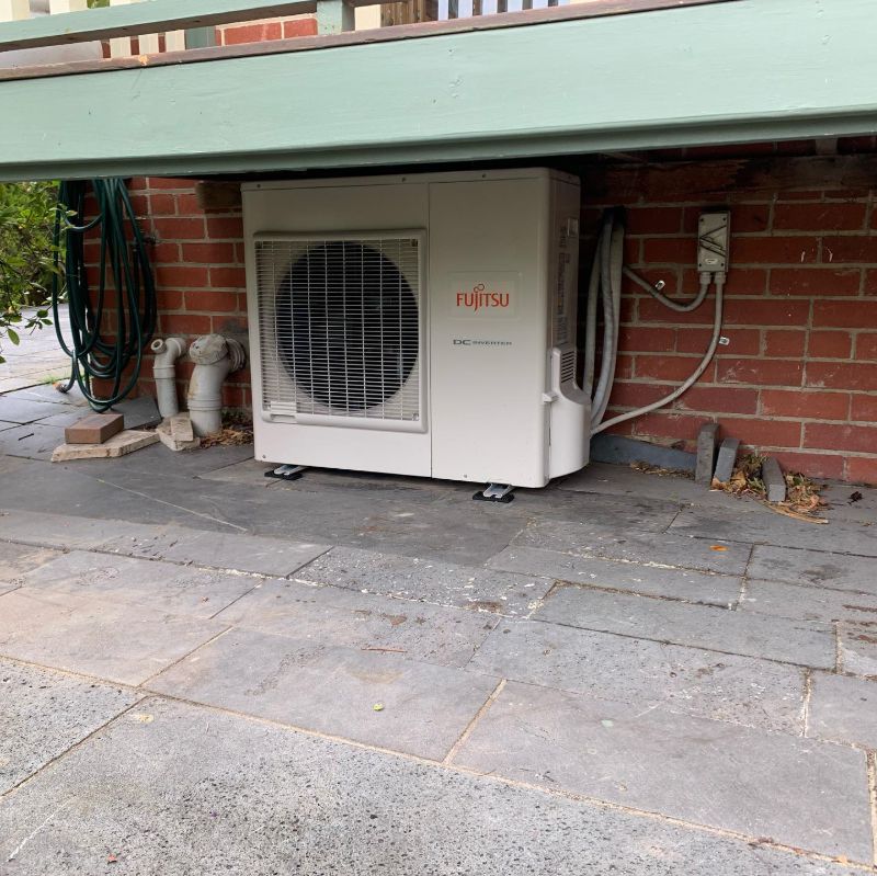 Fujitsu outdoor unit on a paved area beneath a deck