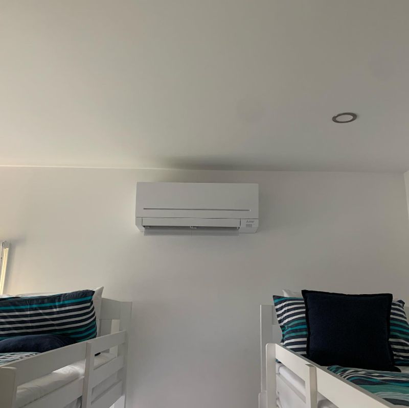 Split system air conditioner above two single beds in a white bedroom