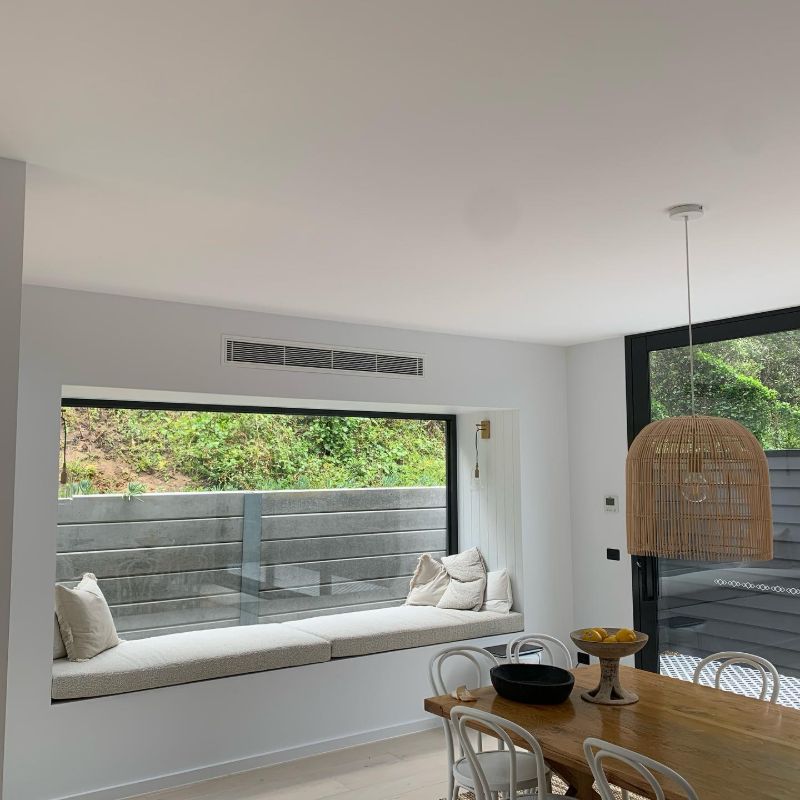 Ducted air conditioning vent above a window seat in a bright dining area