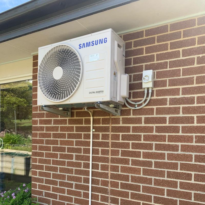 Samsung outdoor unit on wall brackets with its isolator switch on a brick wall