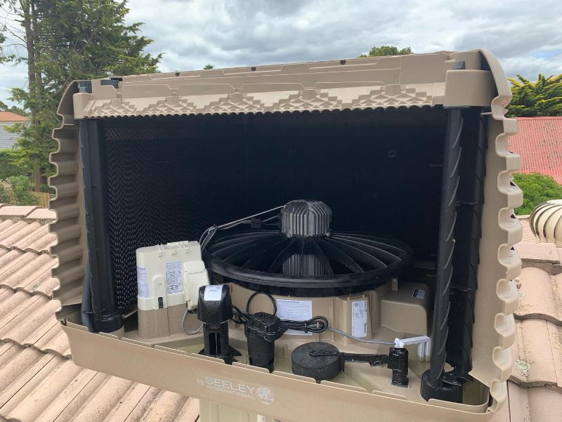 Seeley evaporative cooler opened up on a tiled roof, showing its fan and pump