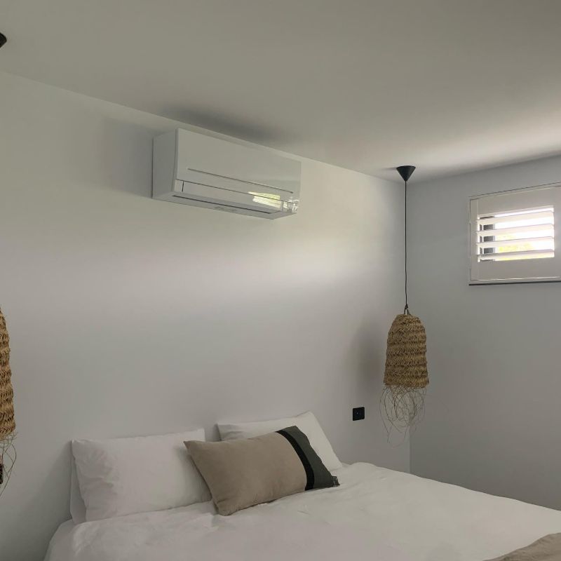Split system air conditioner above a bed with a woven pendant light