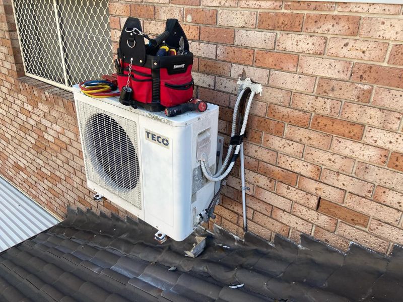 TECO outdoor unit on a tiled roof with a technician's tool bag on top