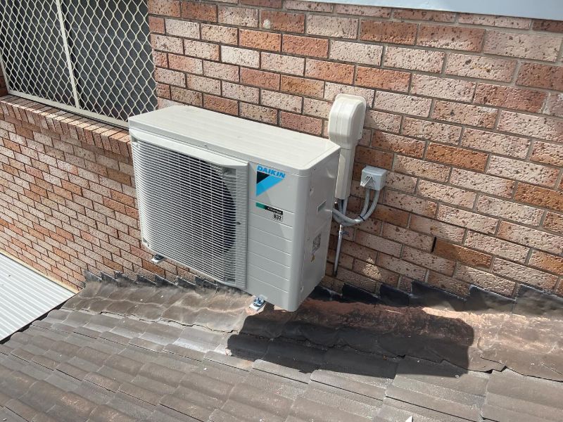 Daikin outdoor unit on a tiled roof against a brick wall