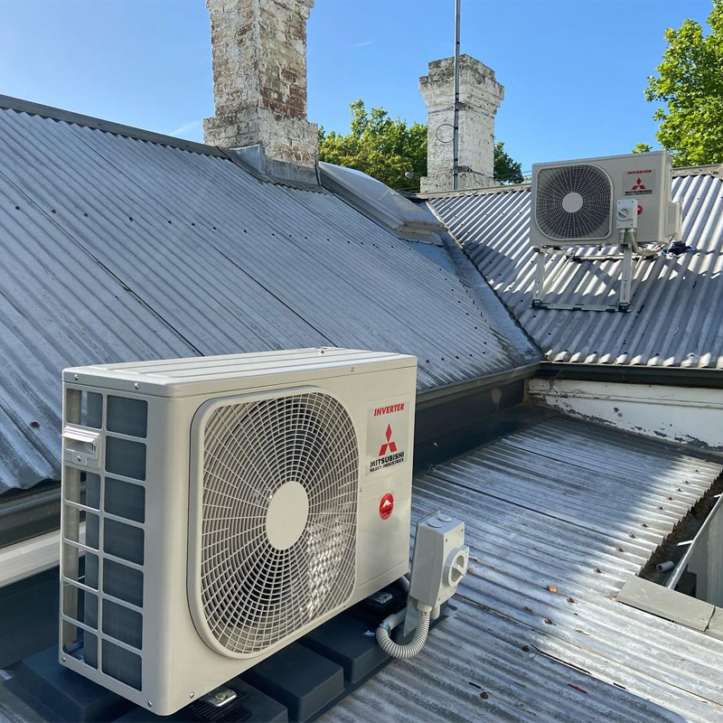 Two outdoor air conditioning units on a corrugated iron roof beside old chimneys