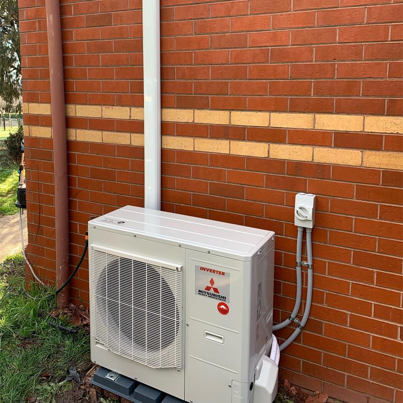 Outdoor air conditioning unit on a slab beside a red brick wall
